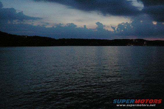 Lake and tree-lined shore under a cloudy dusk sky. Text overlay reads SUPERMOTORS