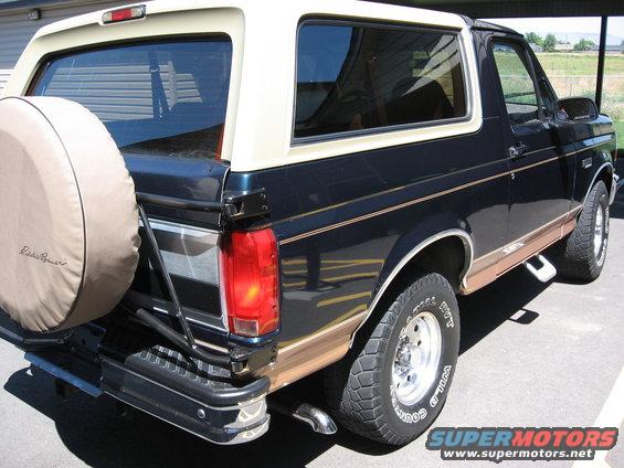 Dark blue Ford Bronco with a tan top and a spare tire on the back. Eddie Bauer badging visible