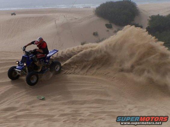 Blue ATV kicking up sand on a dune with a rider