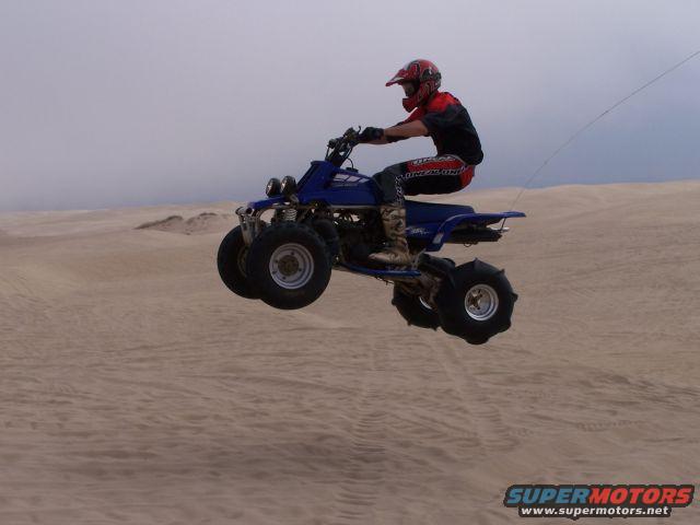 Blue ATV with rider in red helmet jumping over sand dunes