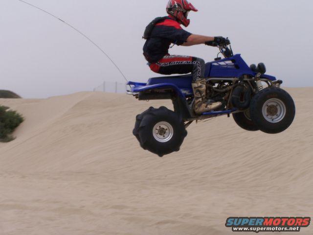 Rider on blue ATV airborne over sand dunes