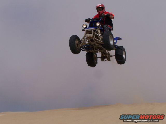 Blue ATV mid-air jump, rider in red helmet and shirt