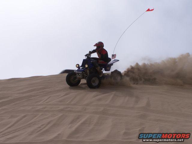Rider on quad bike kicking up dust on a sand dune with an American flag and a red flag