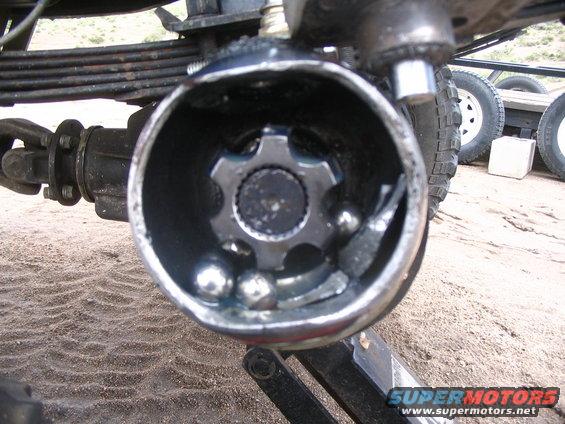 Broken CV joint with loose ball bearings and damaged cage. Part of a leaf spring and driveshaft visible