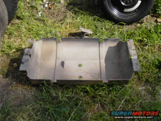 Metal undercarriage part on grass, with tire in background