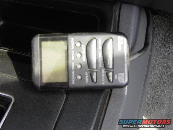 Portable CD player with buttons for program, scan, repeat, random, disc select, display, track skip, search, play/pause, and off. It's sitting in a car's center console