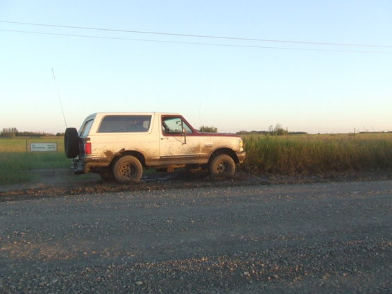 1990 Ford Bronco parked on dirt road, covered in mud, spare tire mounted on rear door