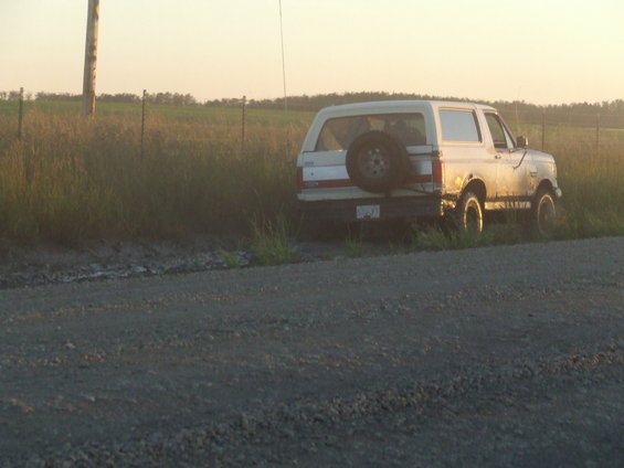 White 1990 Ford Bronco parked on a dirt road with a spare tire on the rear door