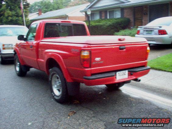 Red pickup truck with a bed cover parked on a street, another vehicle is visible on the left