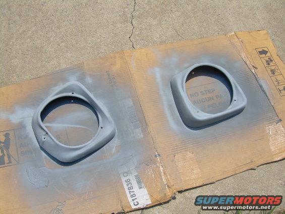 Two gray primer-coated headlight bezels on cardboard