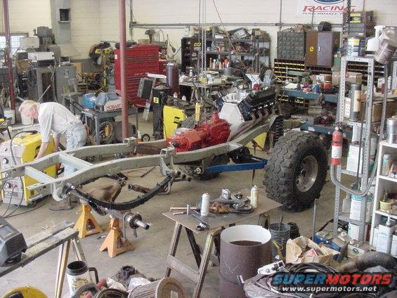 Vehicle frame with engine and large tire in workshop
