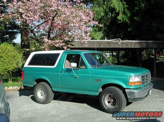 1992 Ford Bronco, green with white top, parked outdoors near trees