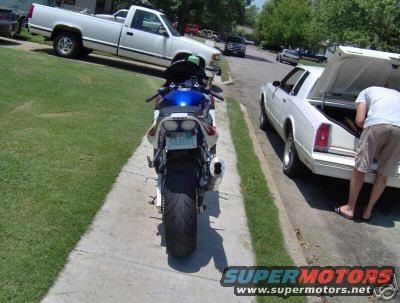 Rear view of a 2001 Yamaha R1 motorcycle parked on a sidewalk next to a white car with an open trunk