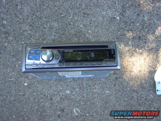 Car stereo with a silver faceplate and a digital display, lying on a concrete surface