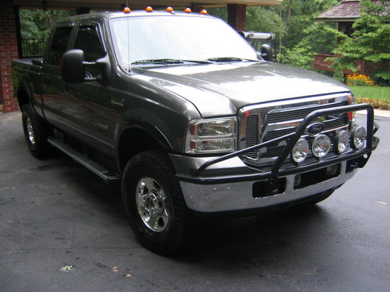 Gray Ford Super Duty pickup truck with a black brush guard and four fog lights parked on a driveway