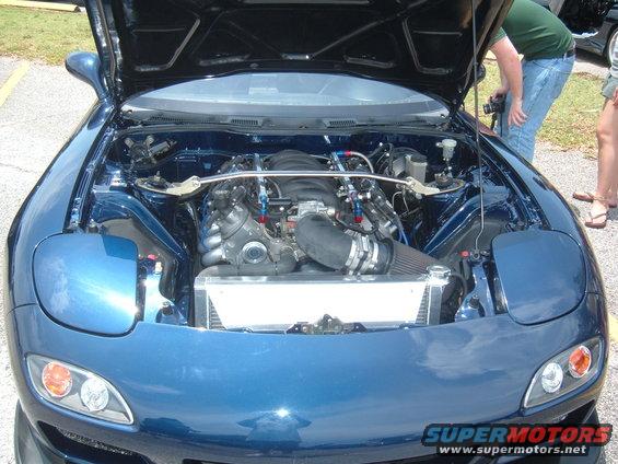 Blue car with hood open showing engine bay and aftermarket engine swap. Radiator and intake are visible