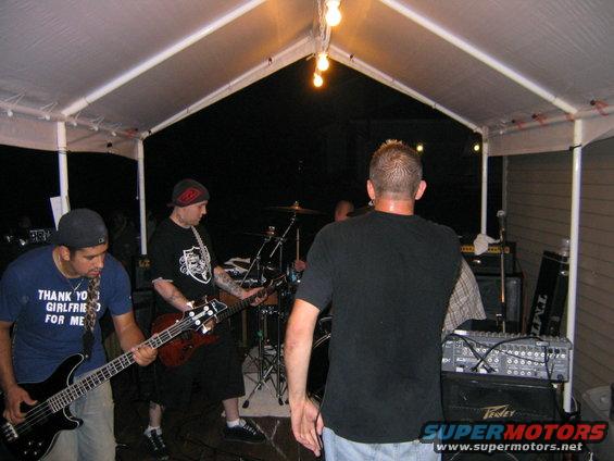 band playing under a tent, one guy wears a shirt that says "THANK YO GIRLFRIEND FOR ME"
