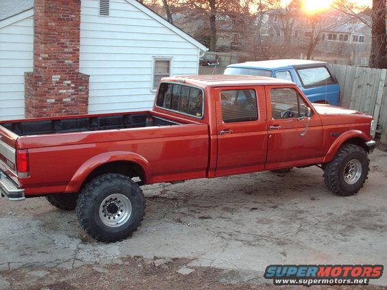 1991 Ford F-350 crew cab pickup truck, lifted, side view. Blue van parked behind