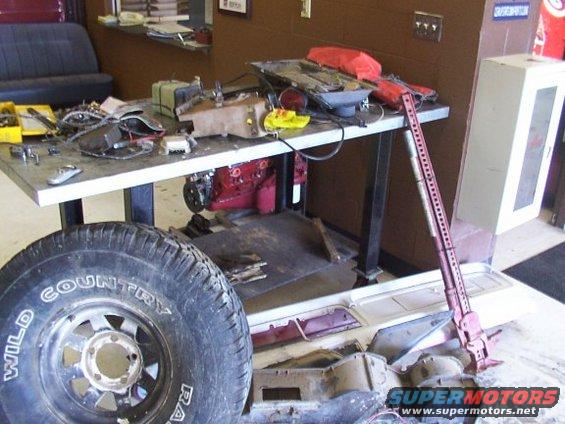 Workbench with parts, tools, and a tire; red Hi-Lift jack