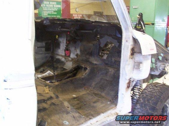 Interior of a vehicle being worked on, showing stripped-down dashboard and floor