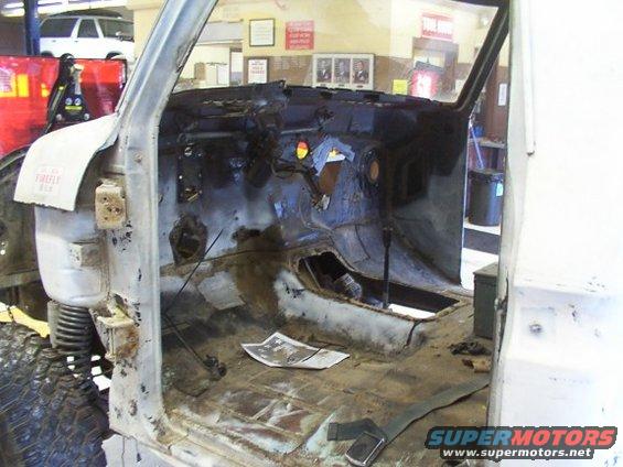 Interior of a stripped-down vehicle showing rusted floor and dashboard removed
