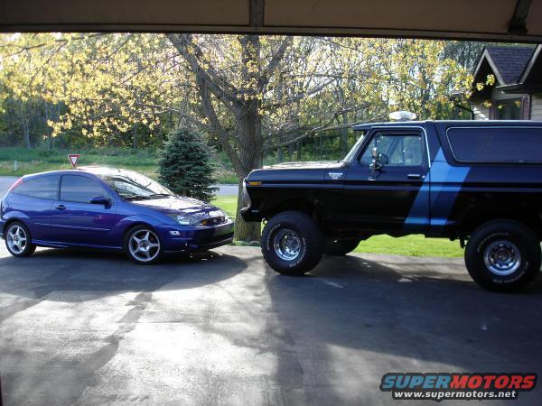 Black 1979 Ford Bronco with blue stripe parked next to a blue hatchback