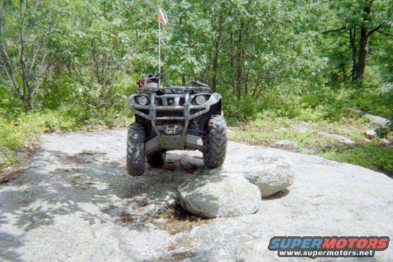 ATV with orange flag on rocks in wooded area