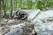 2005 Yamaha GRIZZLY 660 - An all-terrain vehicle carefully maneuvers over large rocks on a wooded trail.