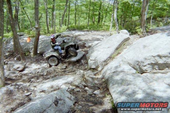 ATV navigating a difficult rocky trail in a wooded area