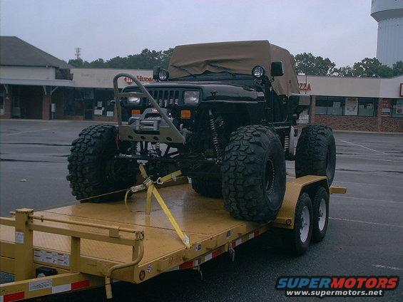 Black Jeep Wrangler on a yellow trailer, front view, with large off-road tires and a winch