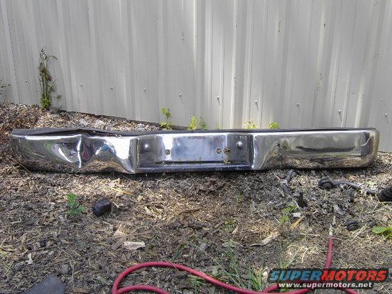 Chrome rear bumper with significant dents and damage, mounted on the ground