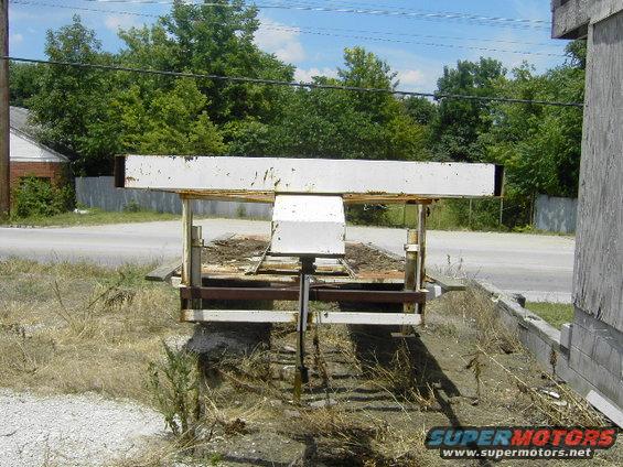 White metal trailer with rusted supports and debris on a dirt lot