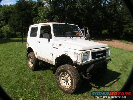 White Suzuki Samurai with off-road tires and a dented front fender