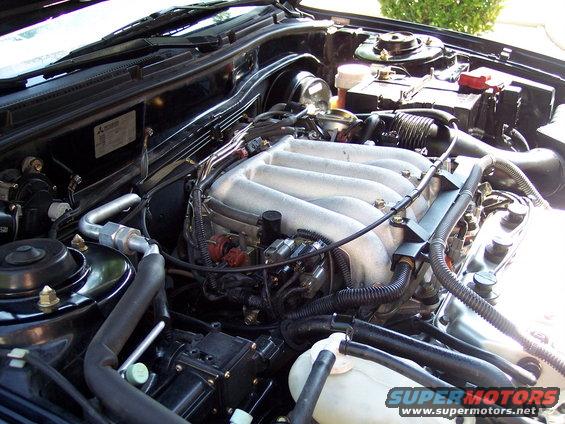 Engine bay with V6 intake manifold, battery, and hoses visible. SuperMotors logo in lower right