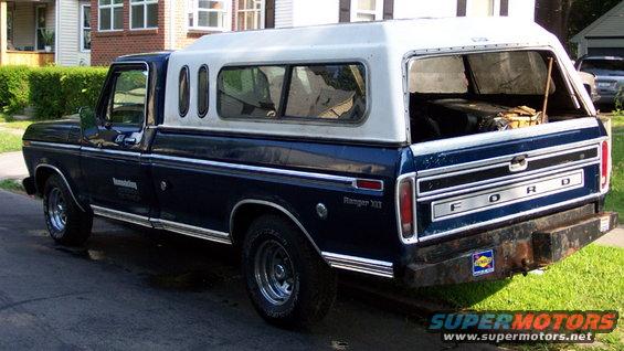 Blue Ford pickup truck with a white camper shell, seen from the rear