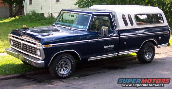 Dark blue 1975 Ford F-150 pickup truck with a white camper shell, parked on a street