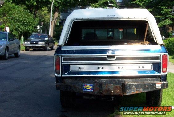Rear view of blue 1975 Ford F-150 pickup with white camper shell and aftermarket bumper