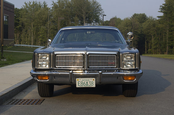 Front view of a dark sedan with a large chrome grille and quad headlights. License plate reads E86A38