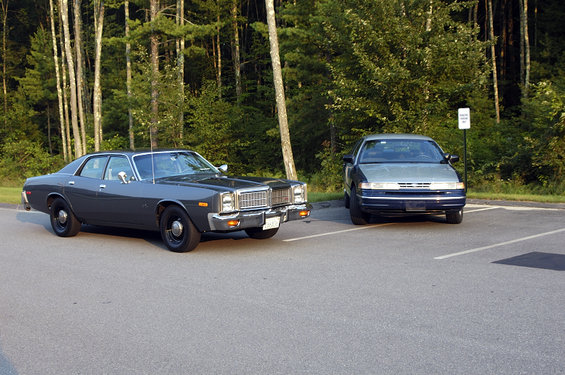 Dark gray sedan parked in a lot, front quarter view. It has a chrome grille and square headlights