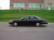1998 Ford Crown Victoria - Side profile of a black 1998 Ford Crown Victoria parked on asphalt in front of a grassy hill and brick building.
