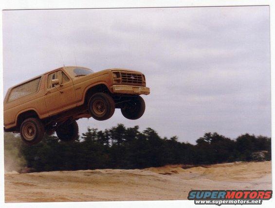Tan Ford Bronco mid-air jump, front 3/4 view, dusty landing zone