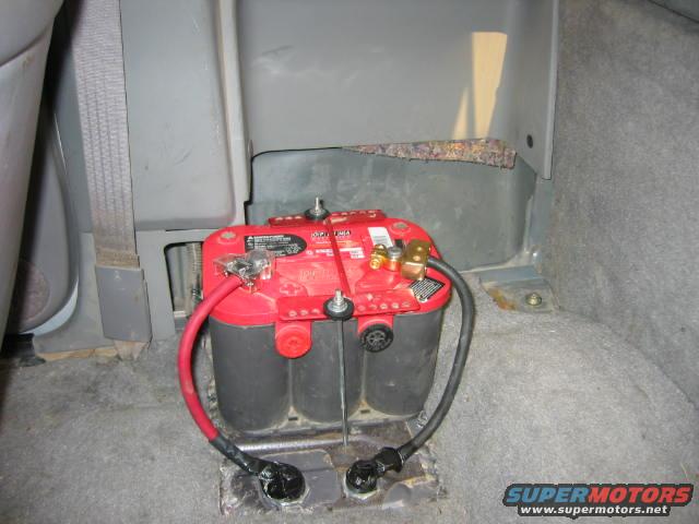 Optima Red Top battery with red and black cables connected, mounted in the rear of a vehicle