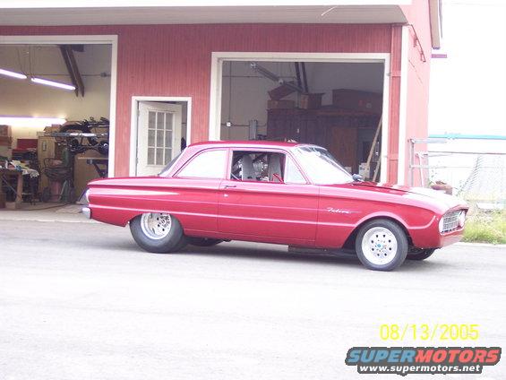 Red 1960 Ford Falcon with racing interior, parked outside a garage