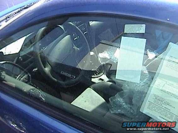 Interior view of a blue car, showing the steering wheel, dashboard, and papers on the windshield