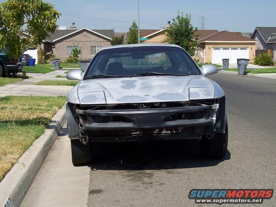 Silver 1993 Ford Probe with missing bumper and primer spots, parked on a residential street