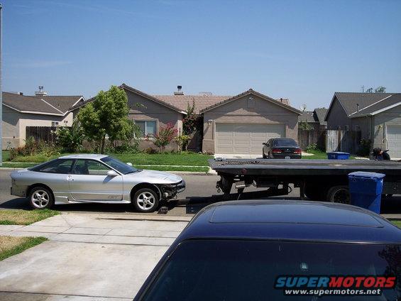 1993 Ford Probe coupe parked on street, front bumper missing, tow truck behind it