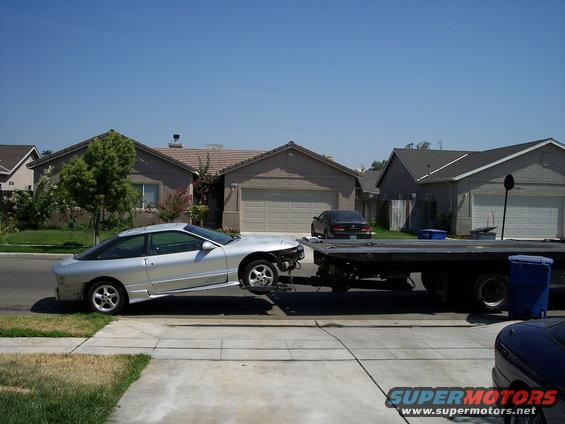 Silver 1993 Ford Probe being towed on a flatbed truck, front bumper missing