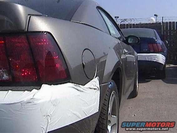 Gray Ford Mustang rear quarter panel with white protective wrap on bumper and fender. Another blue Mustang is parked behind it