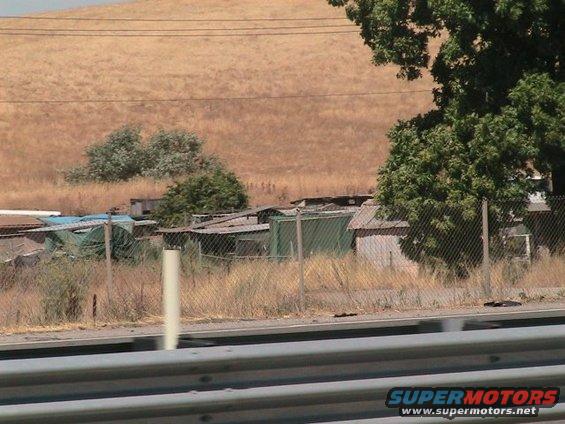Junkyard scene with various structures behind a fence