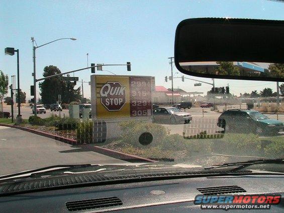 Gas station with Quik Stop sign, cars on road, and a green SUV